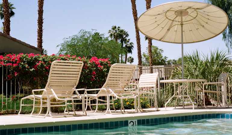 rectangular outdoor pool with sunbathing chairs and umbrellas next to it, surrounded by an aluminium fence