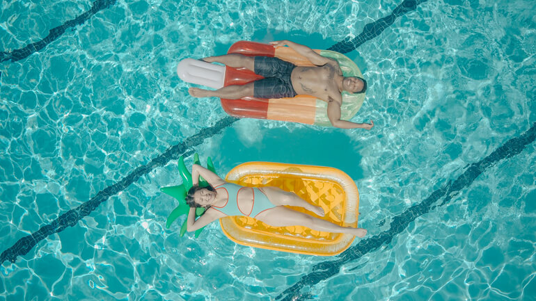 Two people relaxing on inflatable rafts in a swimming pool.