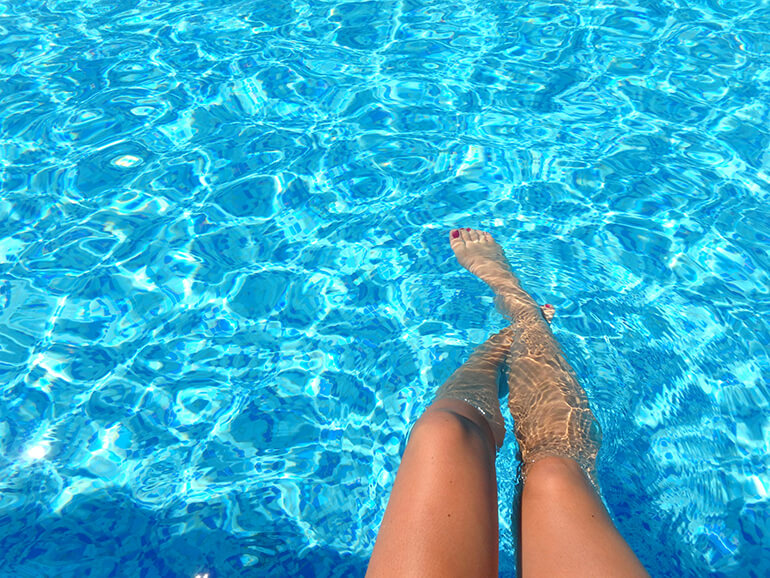 Person's legs in a clear blue swimming pool.